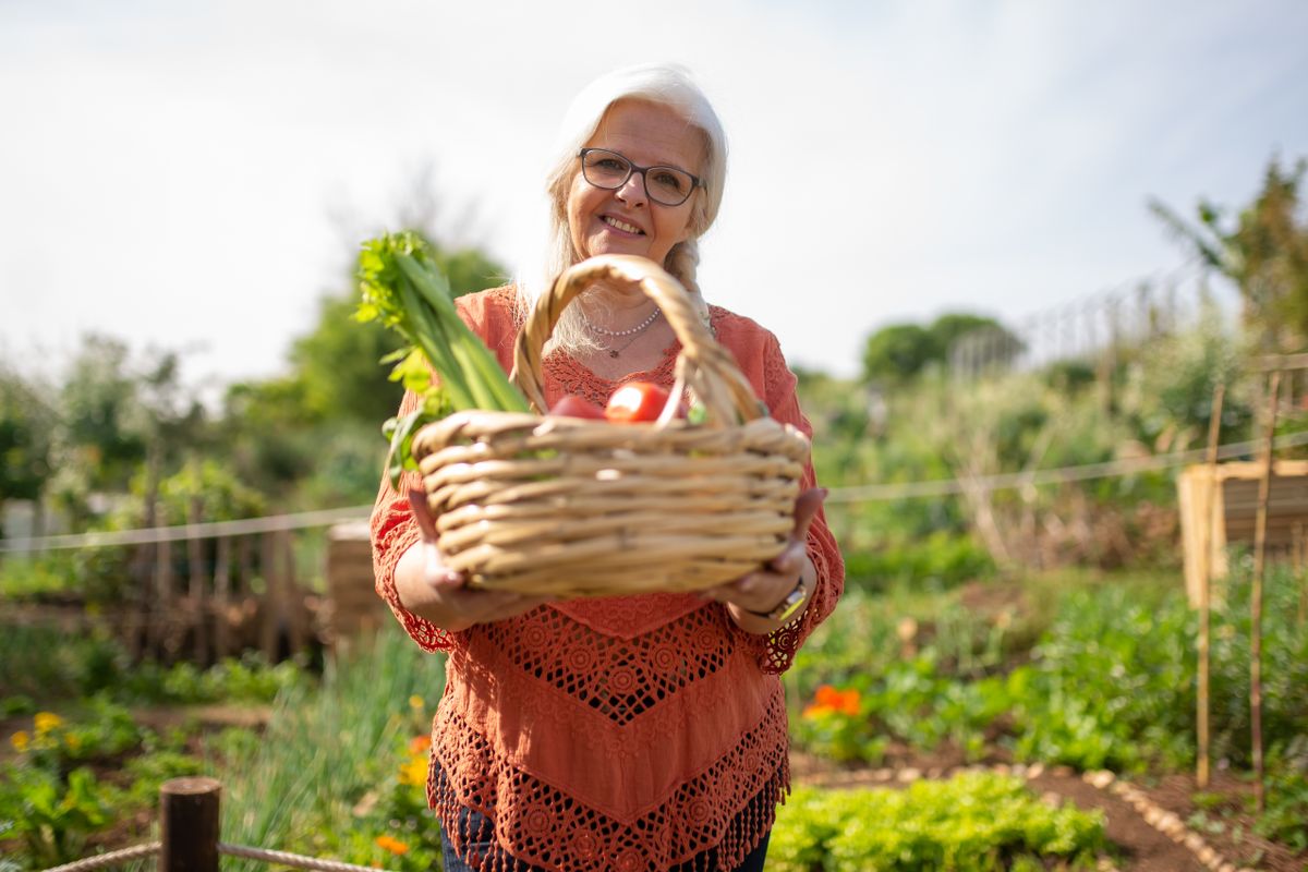 Elderly woman smiling with a basket of fresh vegetables